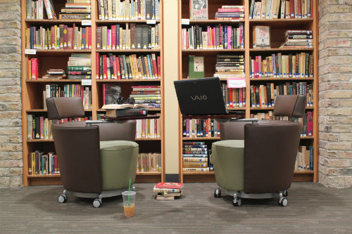 Two chairs in front of book cases. One of the chairs has a laptop computer on a side table.