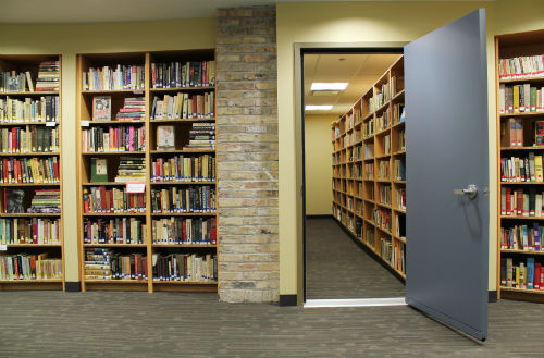 A wall with bookcases and a door that leads into another room with more book cases.